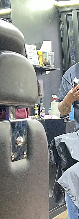 Respaldo de piel negra de la silla de barbero y repisa con productos al fondo