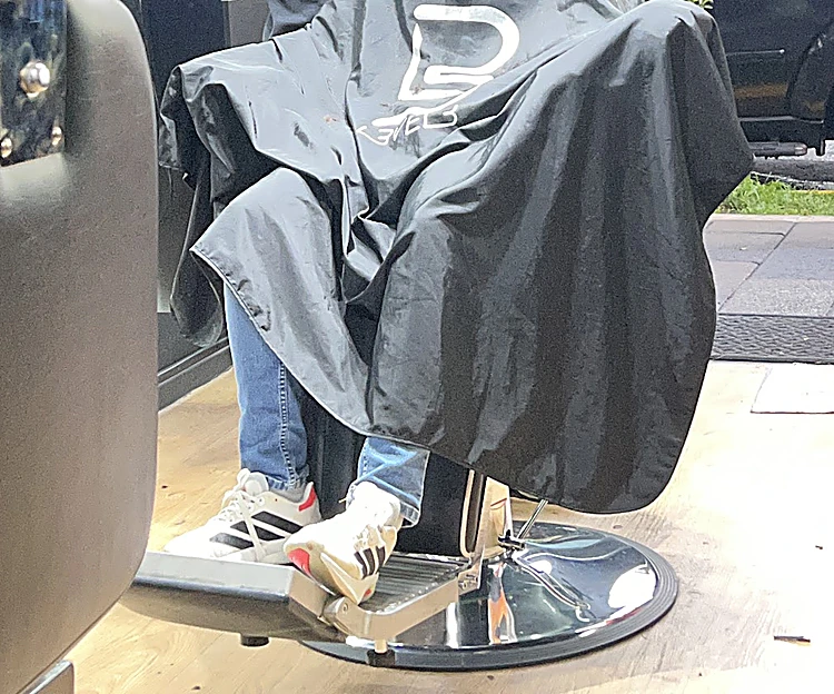 Cliente en la silla de barbero cubierto con la capa negra, visto del pecho hacia abajo, con el reposapiés cromado